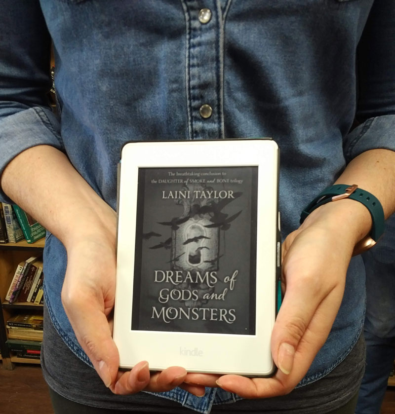 Silent book club participant holds Kindle showing Dreams of Gods and Monsters by Laini Taylor