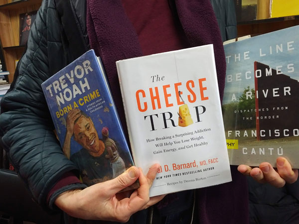 Silent book club participant holds books by Trevor Noah, Dr. Neal Barnard and Francois Cantu