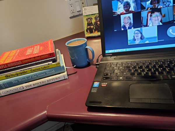Silent book club zoom meeting, with books and coffee cup next to computer