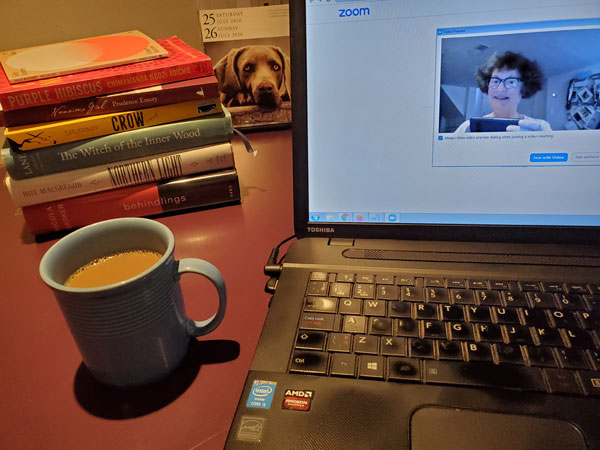 Stack of books, cup of coffee, dog calendar, computer screen showing me getting ready for book club zoom meeting