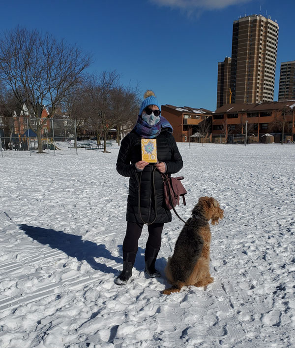 Me in the snowy park holding a book, while Tilly the Airedale looks elsewhere