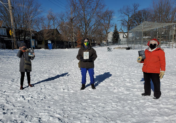 Three silent book club  members standing in the snowy park with their books
