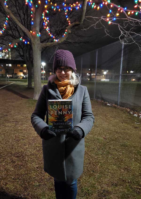 Silent book club member Catherine in the park, with a book by Louise Penny