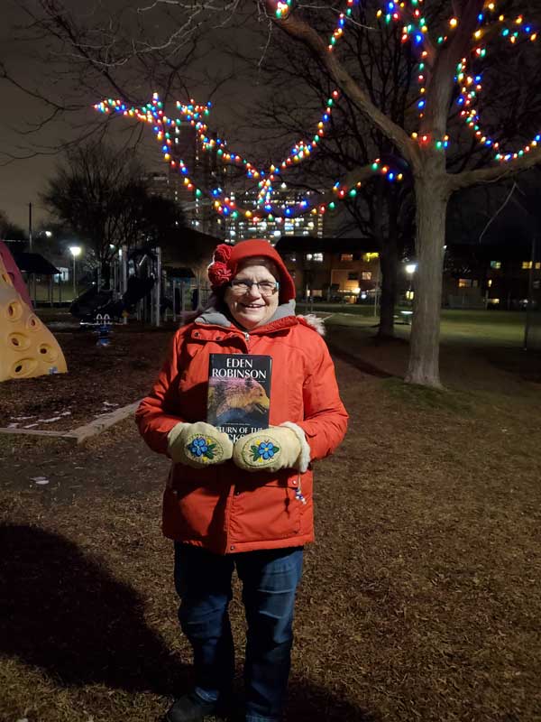 Silent book club member Jo in the park, with a book by Eden Robinson
