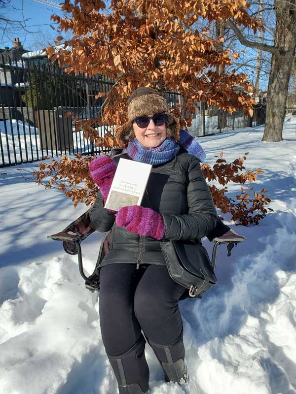 Silent book club member Vicki sitting in a chair in snowy Stephenson Park, holding a book by Tolu Oloruntoba