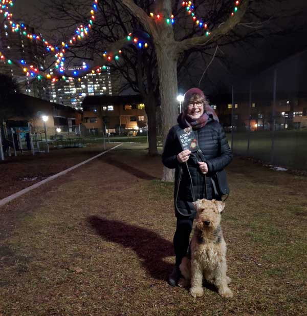 Silent book club member Vicki in the park, with Tilly the Airedale and a book by Doireann Ni Ghriofa