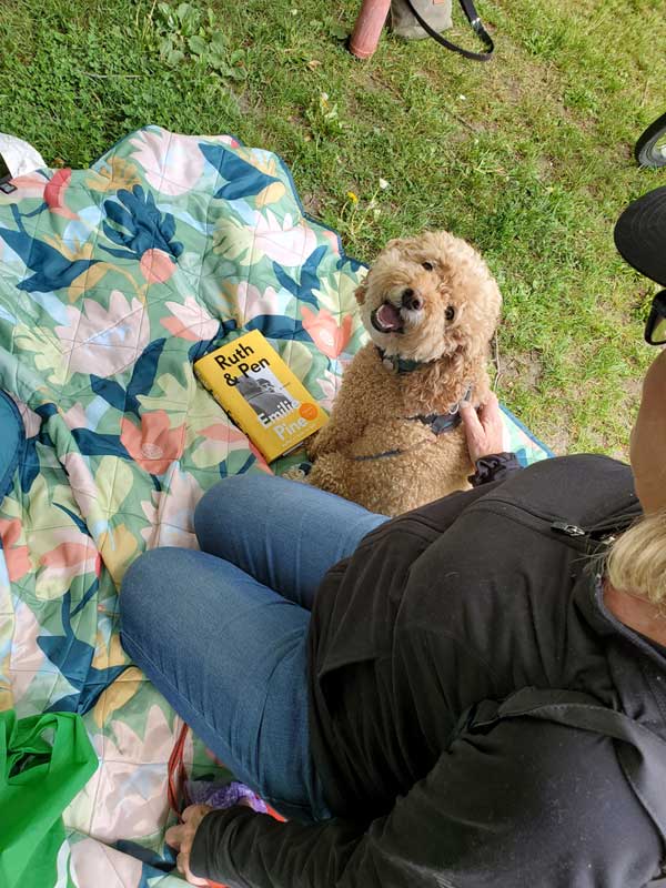 Sue W in the park with Ruby the cockapoo and a book