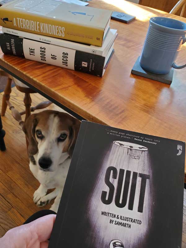 Vicki's stack of books, including The Books of Jacob, with Jake the beagle-basset under the table