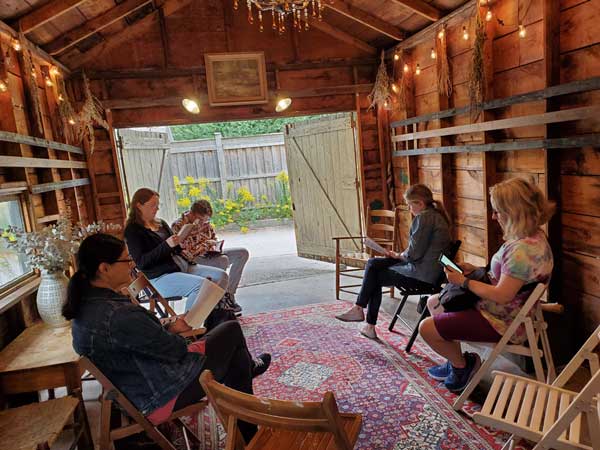 The silent book club group assembles in The Great Escape garage, with the back garage doors open and a chandelier and fairy lights overhead.
