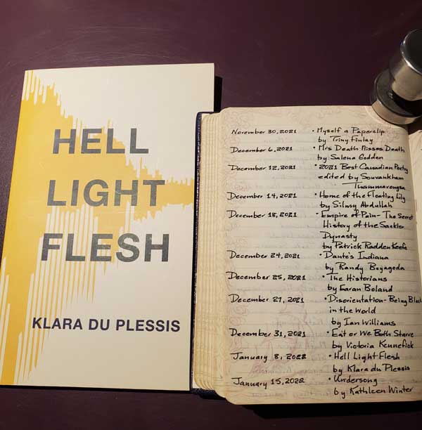 My 2022 year in reading, reflected in a page of my handwritten Book of Books, next to the poetry collection Hell Light Flesh by Klara du Plessis