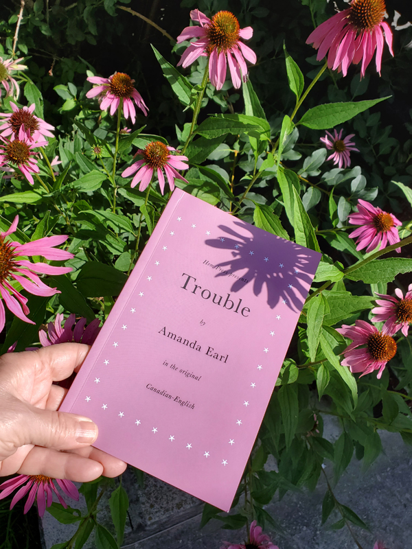 Poetry work Trouble by Amanda Earl, held up amidst pink echinacea