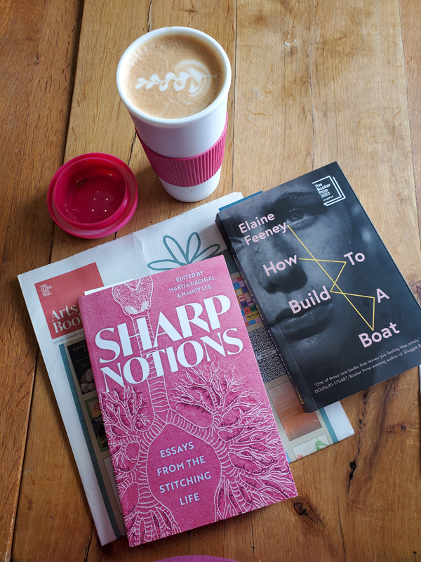 Sharp Notions essay collection and How to Build a Boat by Elaine Feeney sits on wooden table with a latte in a pink and white cup.