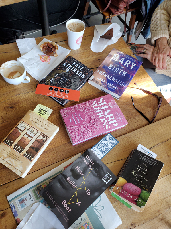 Books, coffee and pastries wonderfully strewn across a table at the East Toronto Coffee Co. Titles include How to Build a Boat by Elaine Feeney and The Magic Mountain by Thomas Mann. Poking out of the books are bookmarks from Type Books, Book City, Biblioasis and the Toronto Public Library.