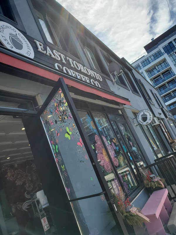 Front of the East Toronto Coffee Co coffee shop, where we hold our Toronto silent book club in-person meetings - The windows are decorated with bright line drawings of flowers and a pink bench is visible near the main door