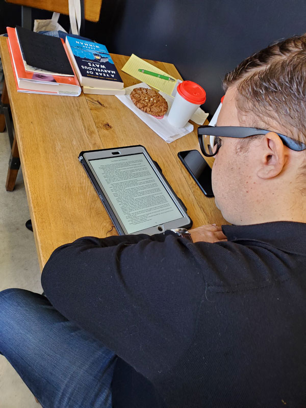 Silent book club member Tom is engrossed in his reading on a tablet, sitting at a wooden table at East Toronto Coffee Co