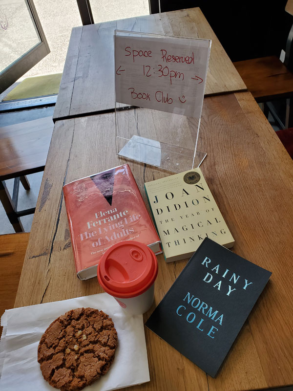 At East Toronto Coffee Co with books by Norma Cole, Joan Didion and Elena Ferrante on the wooden table, along with latte and cookie, ready for silent book club meeting