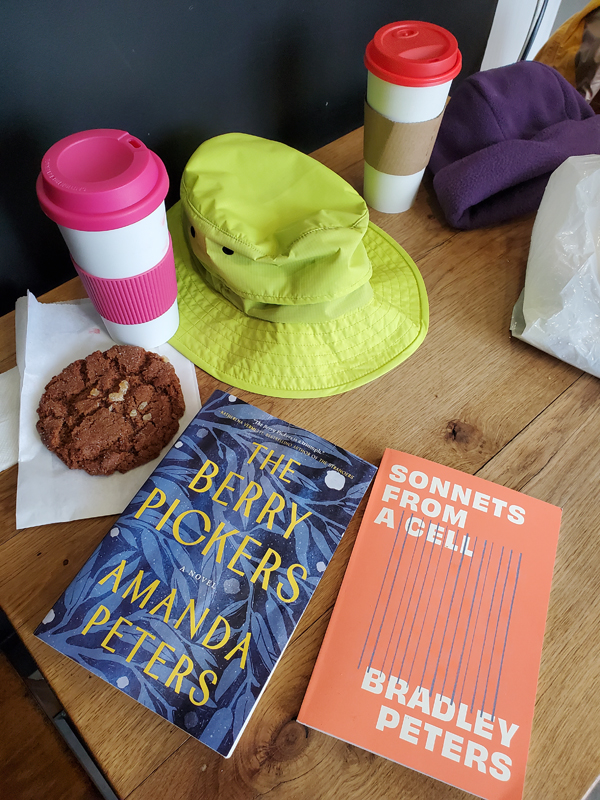 At East Toronto Coffee Co with books by Amanda Peters and Bradley Peters on the wooden table, along with lattes, cookie, bright green and purple hats, ready for silent book club meeting