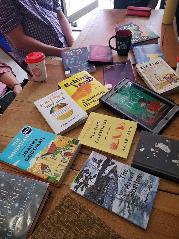 At East Toronto Coffee Co, getting ready for a silent book club meeting, with books by Eden Robinson, Joanna Goodman, Melanie Marttila, Saeed Teebi and more on the wooden table, along with refreshments