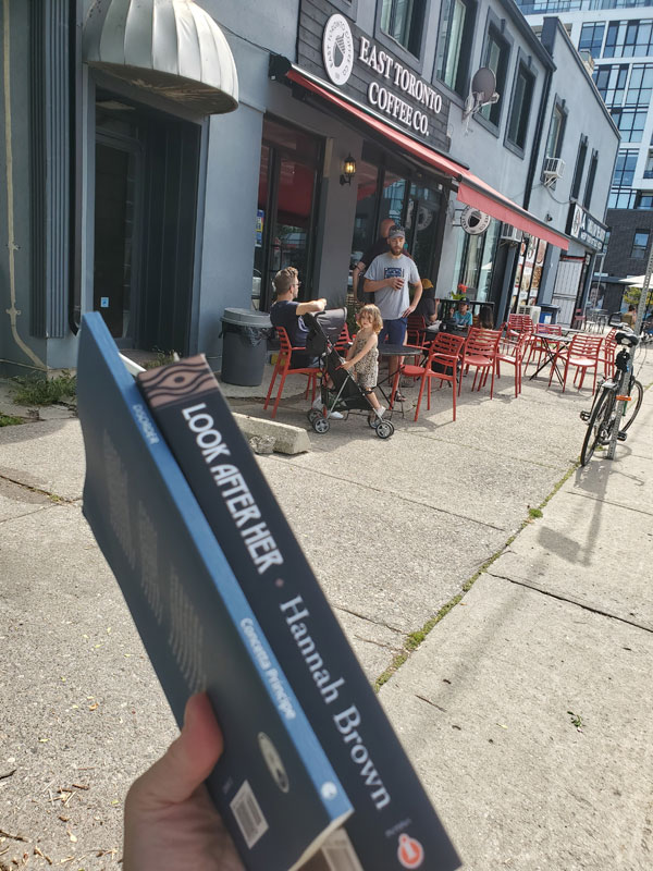 Standing outside the East Toronto Coffee Co coffee shop, holding two books: Look After Her by Hannah Brown and Disorder by Concetta Principe.