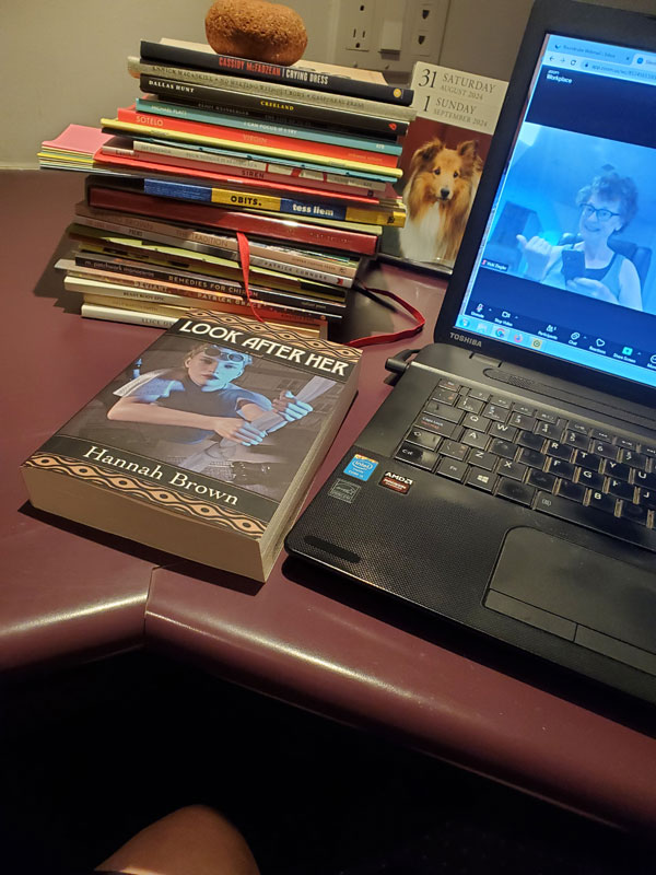 Silent book club member Vicki (that's me, with my signature messy hair and glasses), on screen getting ready for our zoom meeting, with books stacked next to my computer, including a stack of poetry collections I read during the Sealey Challenge, plus the novel Look After Her by Hannah Brown.