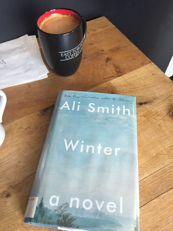 Silent book club meeting at the East Toronto Coffee Co, with one of the group's book selections - Winter by Ali Smith - sitting on a table next to a latte.