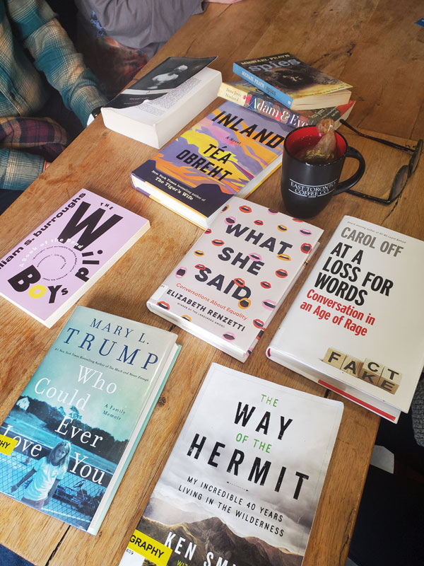 Silent book club meeting at the East Toronto Coffee Co, with some of the group's book selections spread out on the table along with beverages and pastries. The books include works by Carol Off, Elizabeth RenzeETCC merchtti, Tea Obreht, Mary L. Trump + more