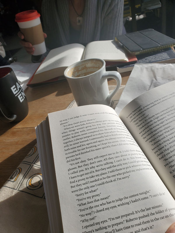 Silent book club members gathered, reading silently, at a table at East Toronto Coffee Co. Afternoon light streaks across book pages ...