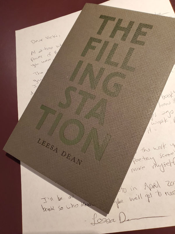 Poetry collection The Filling Station by Leesa Dean (Gaspereau Press), with its striking dark gray and green cover, sits atop a handwritten letter