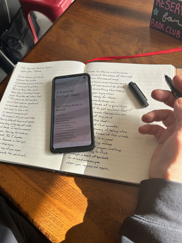 Transcribing a Rachael Boast poem during the silent reading portion of the silent book club meeting at East Toronto Coffee Co. Afternoon light shines across the table.