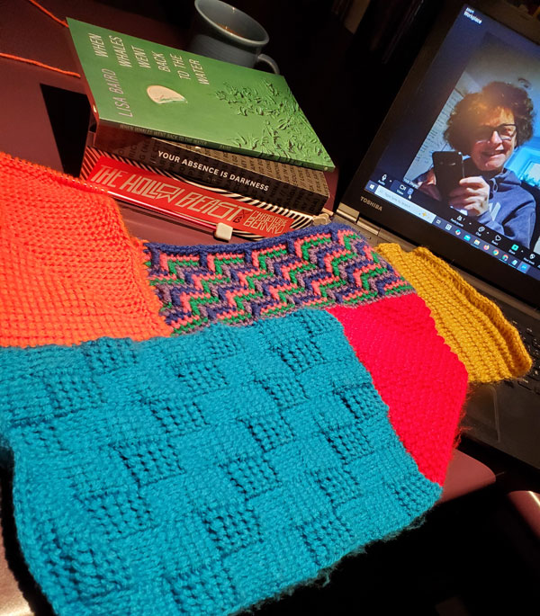 Me (Vicki), on-screen, getting ready for the silent book club zoom meeting, with my books piled next to the laptop, including Your Absence is Darkness by Jon Kalman Stefansson, translated by Philip Roughton, along with some colourful crocheting