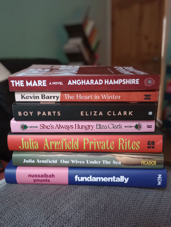Silent book club member Kathyrn's book pile: The Heart in Winter by Kevin Barry, The Mare by Angharad Hampshire, Our Wives Under the Sea by Julia Armfield, Private Rites by Julia Armfield, Boy Parts by Eliza Clark, She's Always Hungry by Eliza Clark, Fundamentally by Nussaibah Younis