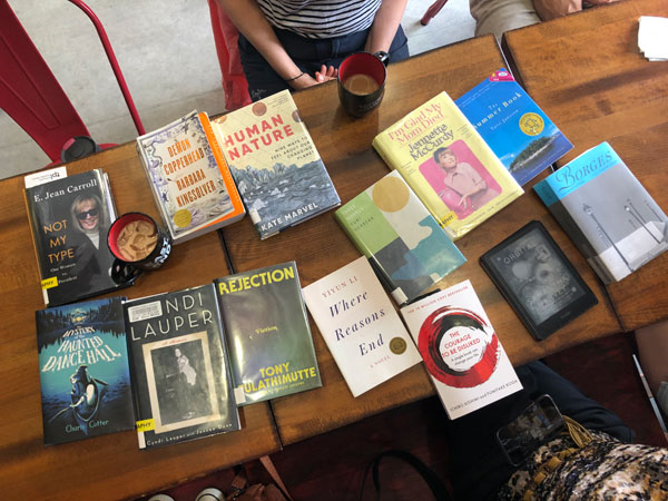 Books and hot beverages and pastries on the table at East Toronto Coffee Co, just before the start of the silent book club meeting - titles include Where Reasons End by Yiyun Li, Cyndi Lauper: A Memoir by Cyndi Lauper with Jancee Dunn, Rejection by Tony Tulathimutte + more - Photo by Jennifer D. Foster