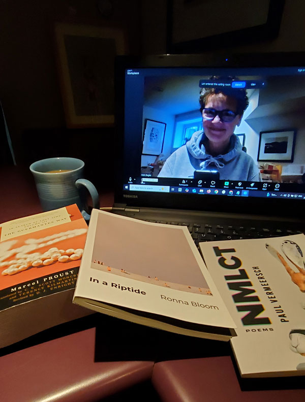 Silent book club member Vicki (that's me, with my signature messy hair and glasses), on screen getting ready for our zoom meeting, with books stacked next to my computer, including works by Marcel Proust, Ronna Bloom and Paul Vermeersch