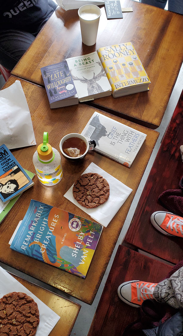 Group book pile at East Toronto Coffee Co, accompanied by coffee and pastries - titles include Remarkably Bright Creatures by Shelby Van Pelt, Intermezzo by Sally Rooney + more (Photo by Vicki Ziegler)