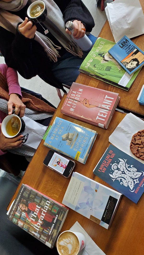 Group book pile at East Toronto Coffee Co, accompanied by coffee and pastries - titles include That Librarian by Amanda Jones, A Marriage at Sea by Sophie Elmhirst, The Tenant by Freida McFadden  + more (Photo by Vicki Ziegler)