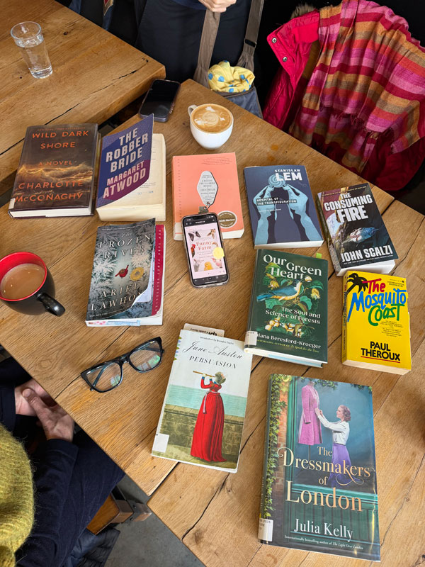 Books spread out on tables at East Toronto Coffee Co, including titles by Margaret Atwood, Paul Theroux, Jane Austen, Julia Kelly + more, accompanied by coffee (Photo by Jennifer D. Foster)