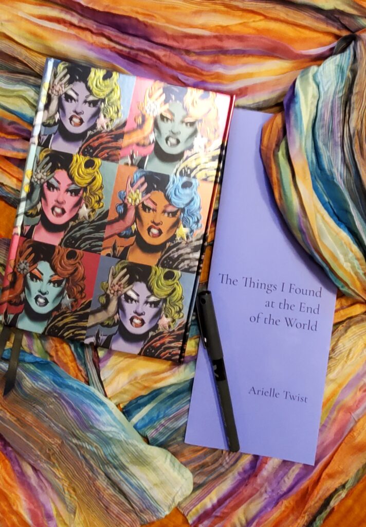 Poetry pamphlet The Things I Found at the End of the World by Arielle Twist (Opaat Press) sits on a colourful scarf with a notebook with a vibrant cover and a fine tip black pen

