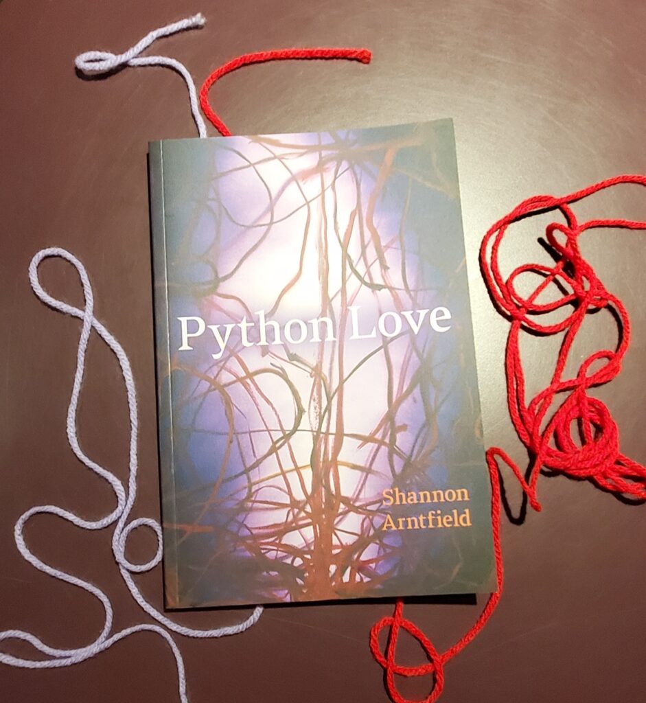 Poetry collection Python Love by Shannon Arntfield (University of Alberta Press) surrounded by loopy strands of red and purple yarn