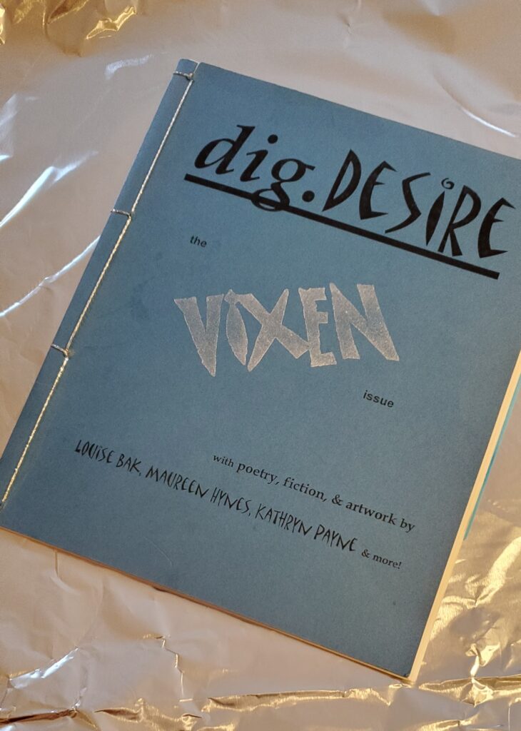 Poetry magazine/chapbook dig.desire Vixen issue (1997 series edited by Jennifer LoveGrove), handmade with blue cover, silver highlights and bound with silver thread, sitting on a background of tin foil