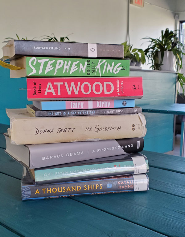 Group book pile at Sprouty Cafe - titles and publications include Doctor Sleep by Stephen King, The Goldfinch by Donna Tartt, Kim by Rudyard Kipling, fairy by Kirby + more (Photo by Vicki Ziegler)