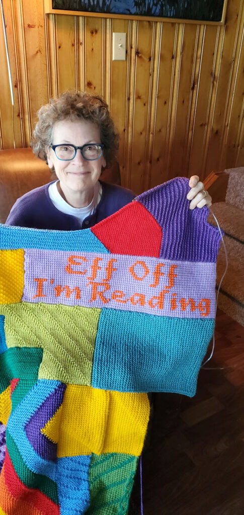 Silent book club member Vicki (me) shows off her crocheted afghan with the embroidered panel that reads